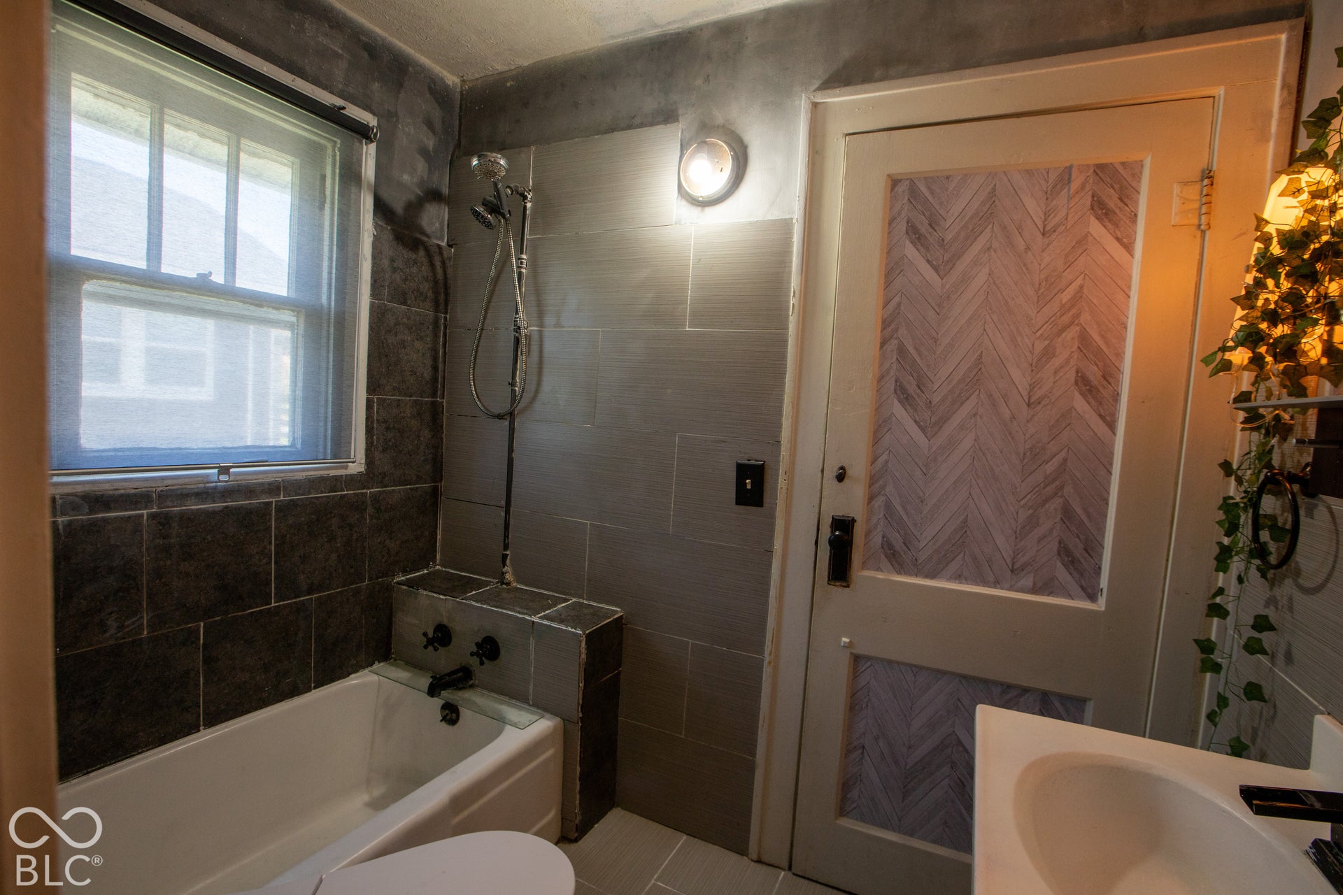 Bathtub with dark tile surround, wall-mounted shower fixture, and a window