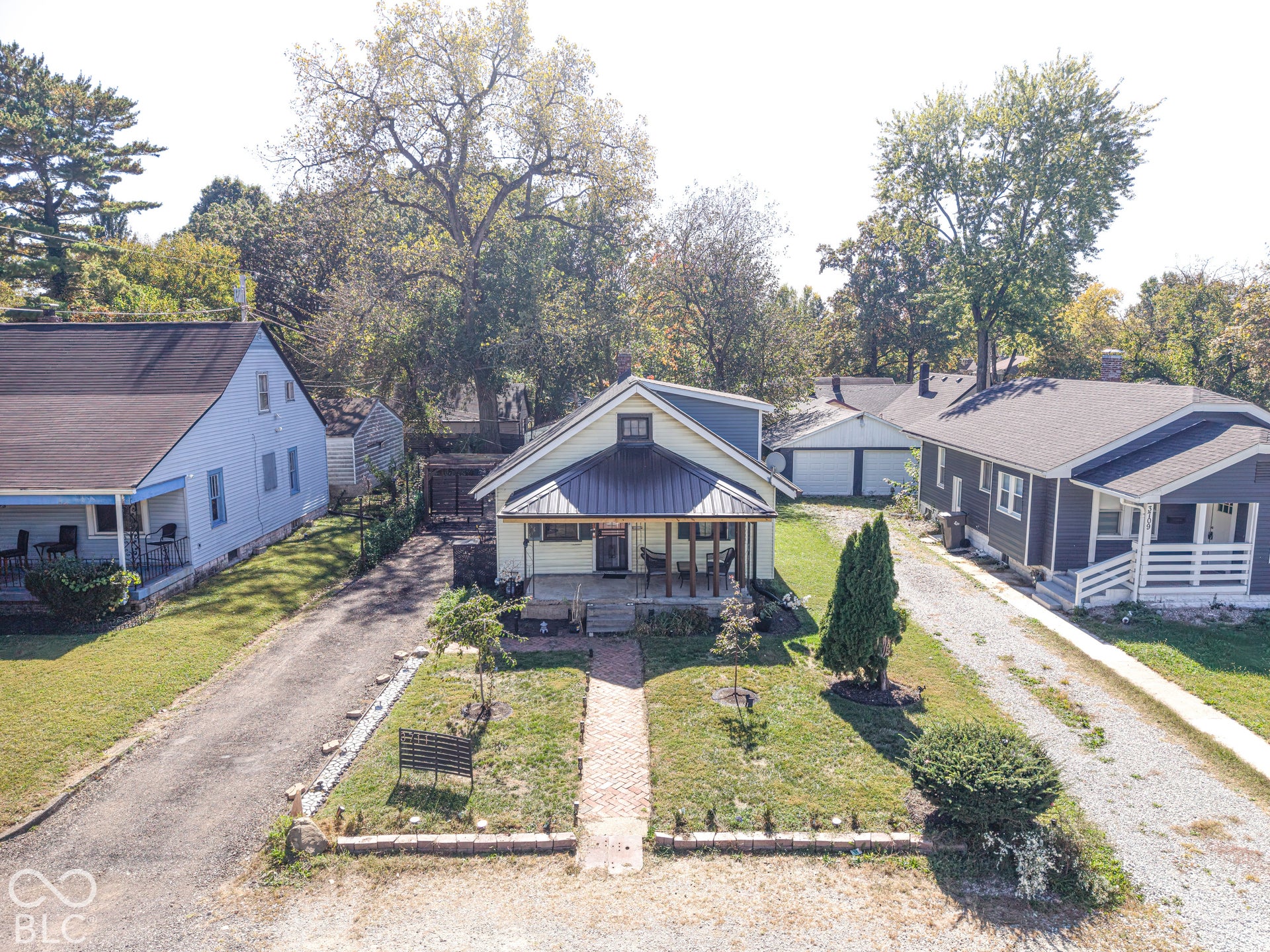 Front porch with metal roof, brick walkway, gravel driveway, and manicured landscaping