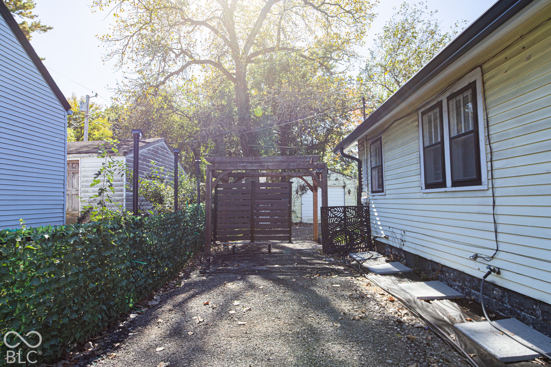 Gravel driveway featuring a decorative wooden pergola and privacy gate
