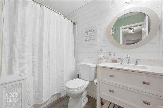 White shiplap wall paneling, vanity with a white countertop, oval mirror, and tiled flooring