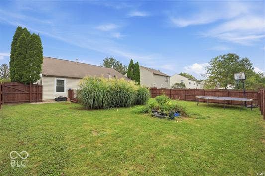 Fenced backyard featuring a manicured lawn, established landscaping, and a wooden deck