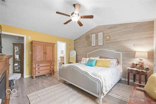 Vaulted ceiling with a ceiling fan, wood-finish flooring, and a decorative accent wall