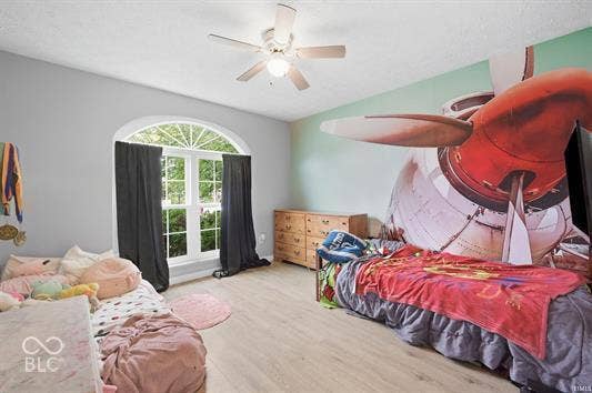 Arched window with grilles, ceiling fan with light, wood-finish flooring, and light gray wall paint