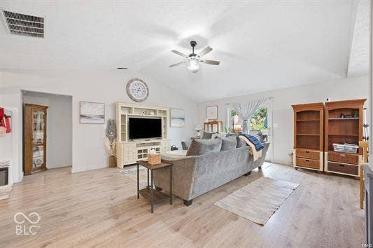 Vaulted ceiling, ceiling fan with light fixture, wood-finish flooring, built-in media console, and an exterior door