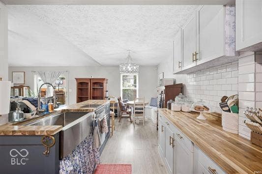 Kitchen featuring wood-finish countertops, white subway tile backsplash, white upper cabinetry, and a large farmhouse-style sink
