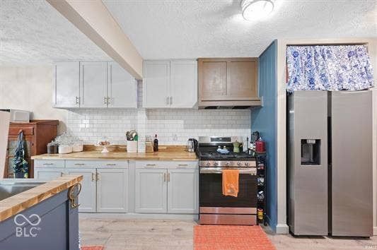 Kitchen featuring light-toned cabinetry, a subway tile backsplash, wood-finish countertops, stainless steel appliances, and wood-finish flooring