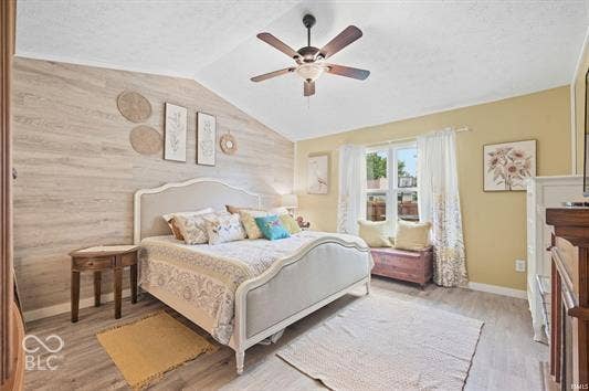 Vaulted ceiling with a ceiling fan, wood-finish flooring, and a decorative accent wall
