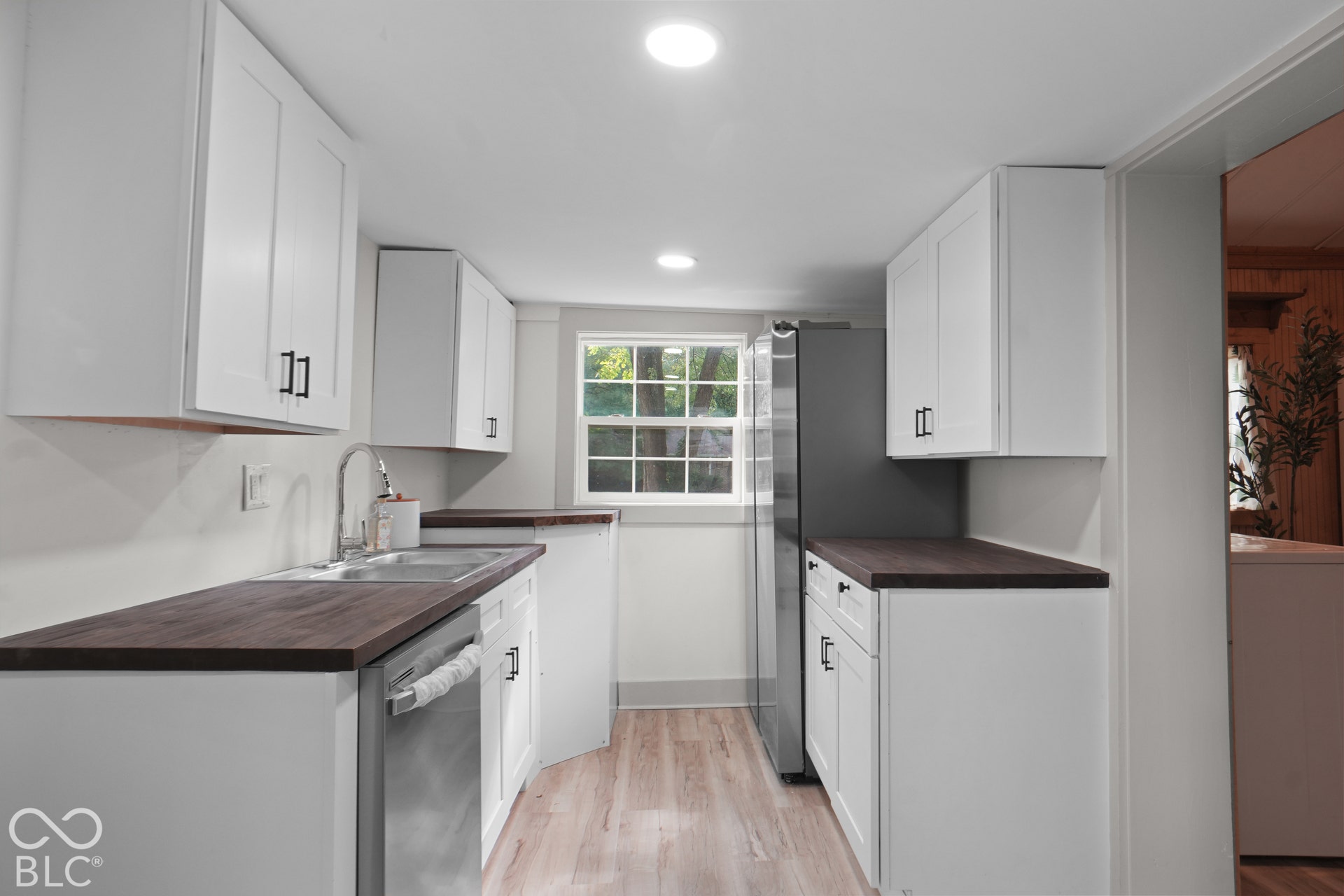 Kitchen featuring white cabinetry with dark hardware, dark wood-finish countertops, stainless steel sink, and wood-finish flooring