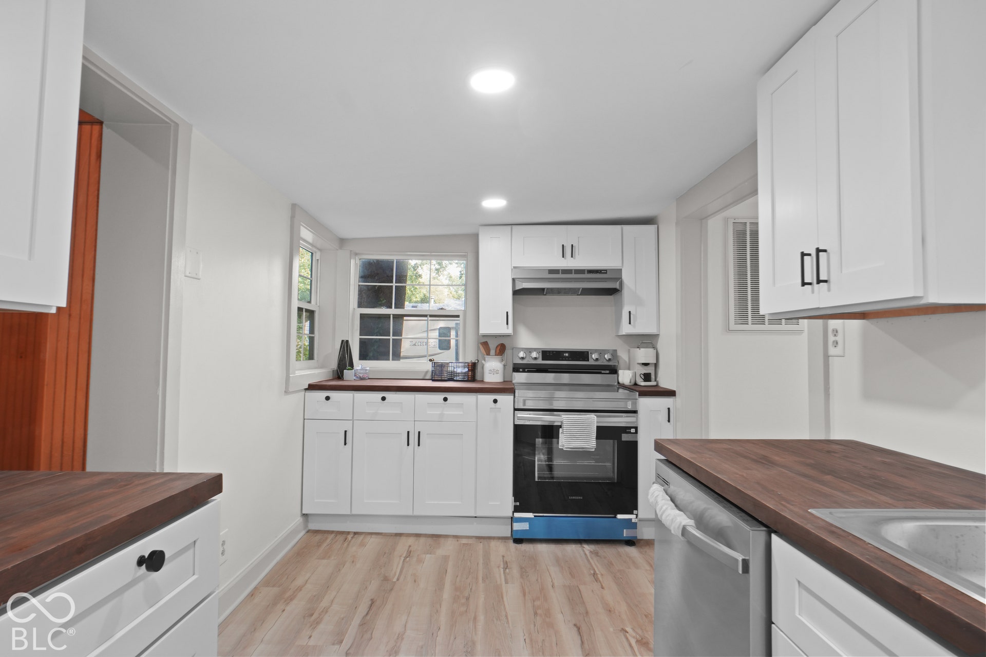 White cabinetry with black hardware, wood-finish countertops, stainless steel appliances, wood-finish flooring, and recessed lighting