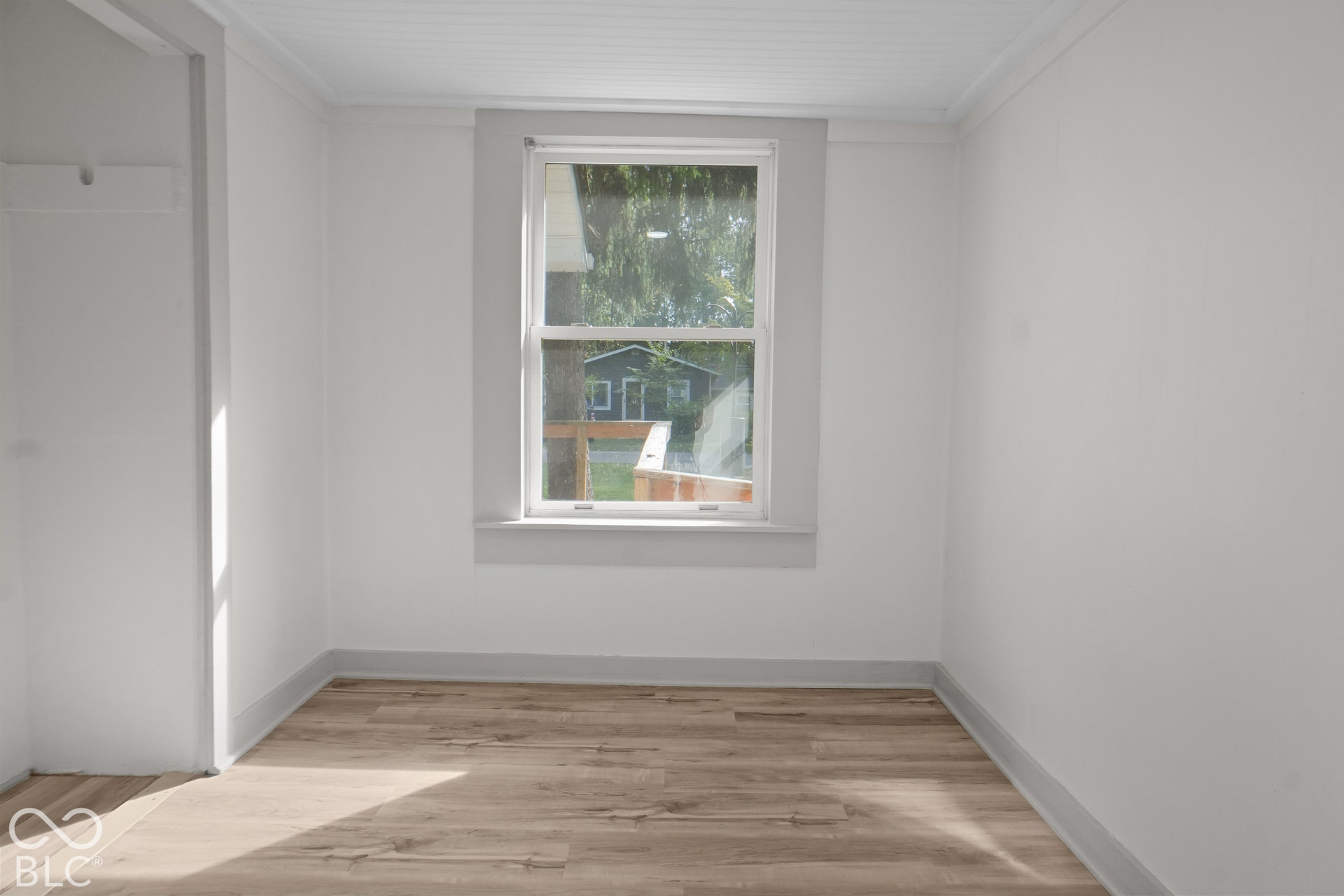 Wood-finish flooring, white walls, and a window with trim