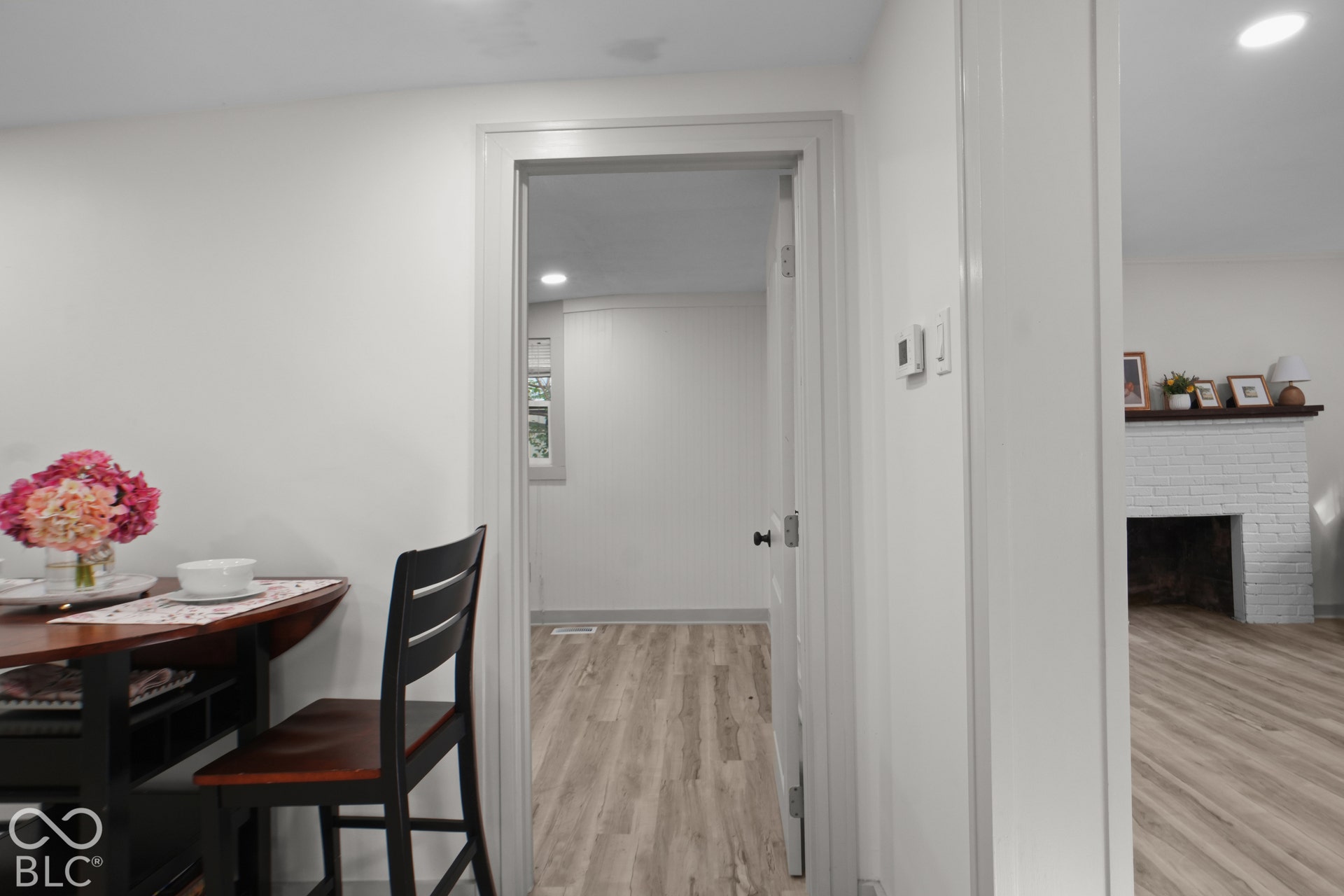 White painted walls, wood-finish flooring, white fireplace, and a window