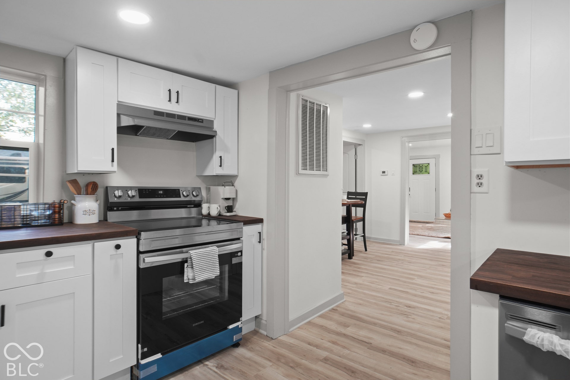 White shaker-style cabinetry with matte black hardware, stainless steel electric range with coordinating range hood, wood-finish countertops, and wood-finish flooring