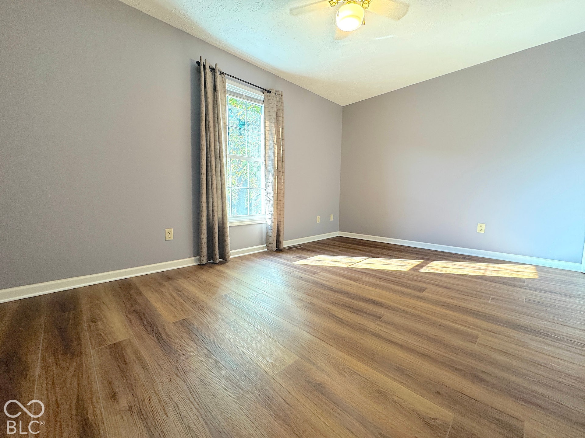 Wood-finish flooring with light gray walls, a ceiling fan, and a window with natural light