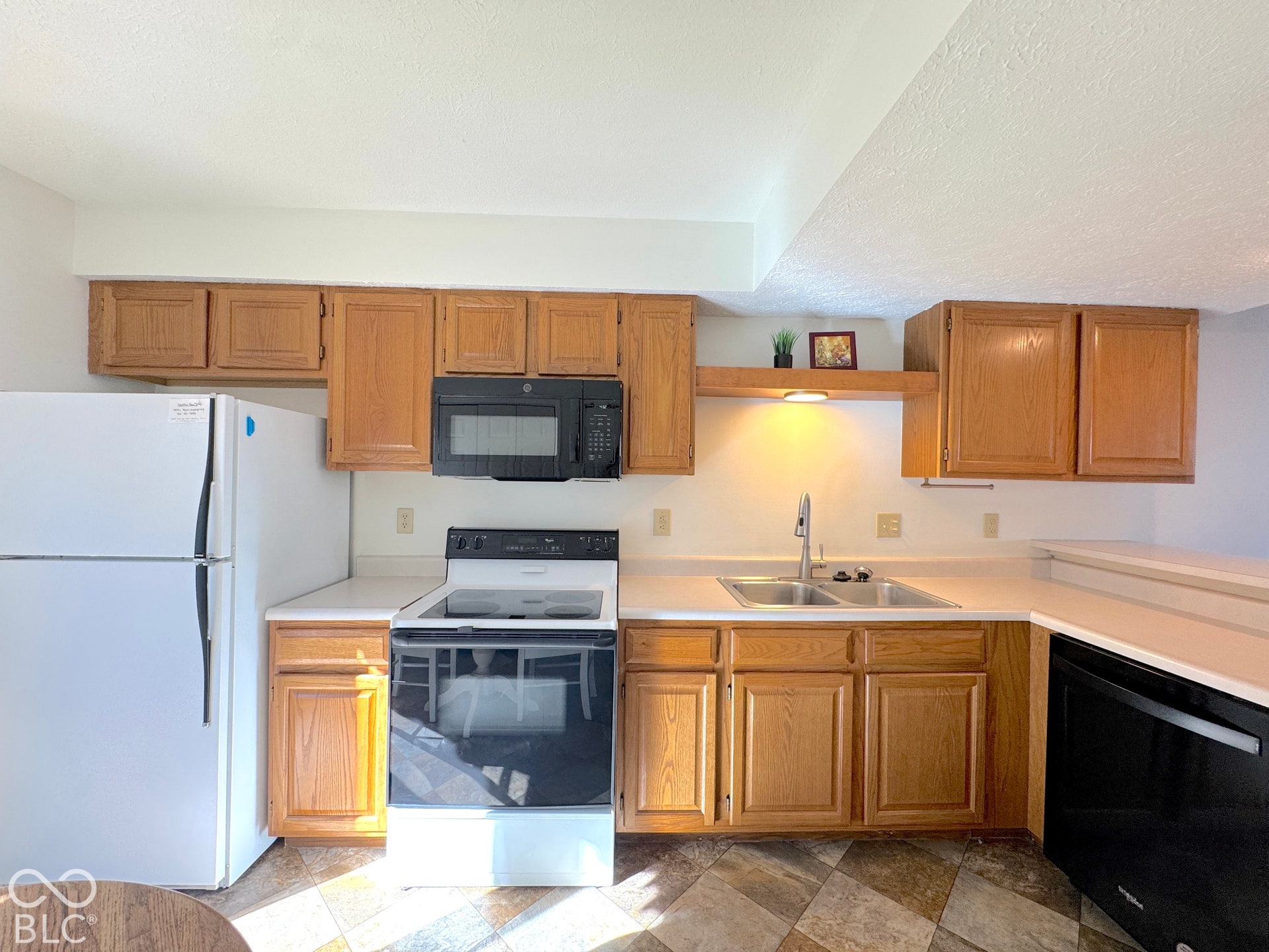 Wood-finish cabinetry, white countertops, stainless-steel double basin sink, and black appliances