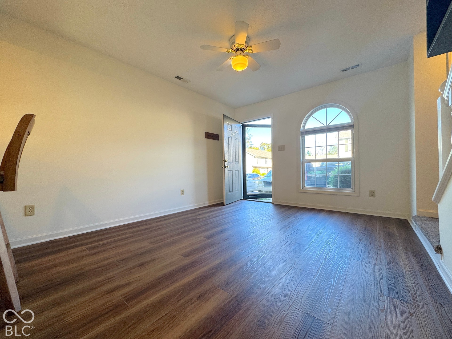 Wood-finish flooring throughout, complemented by a front entry door with transom window, an arched window, and a ceiling fan with integrated lighting