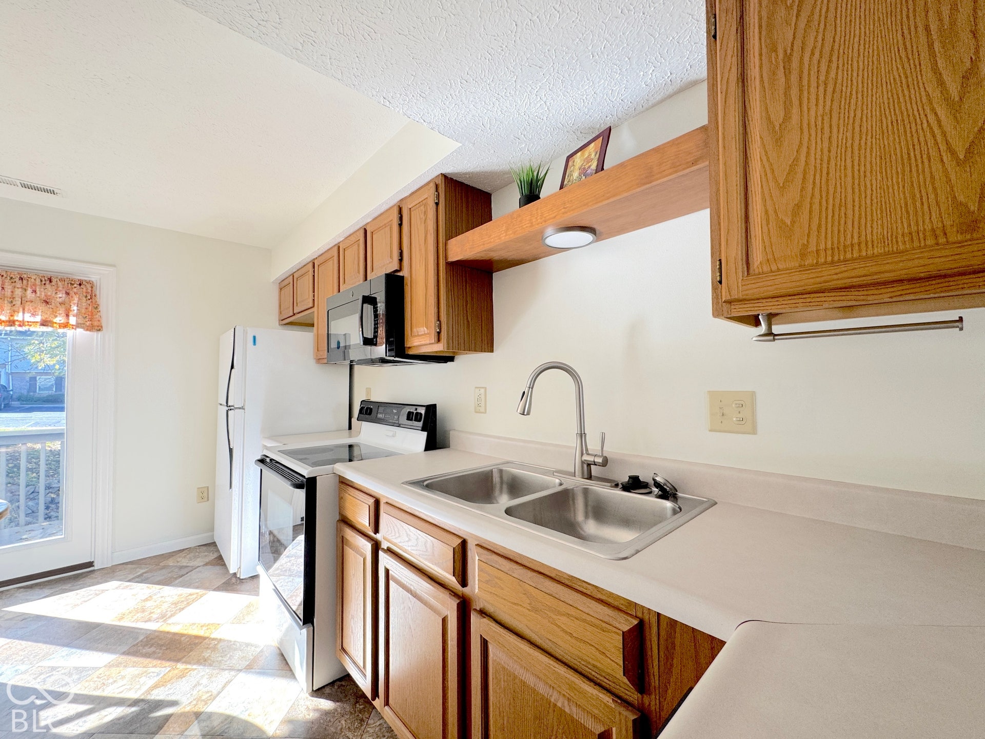 Wood-finish cabinetry, stainless steel double basin sink, stainless steel appliances, and white countertops