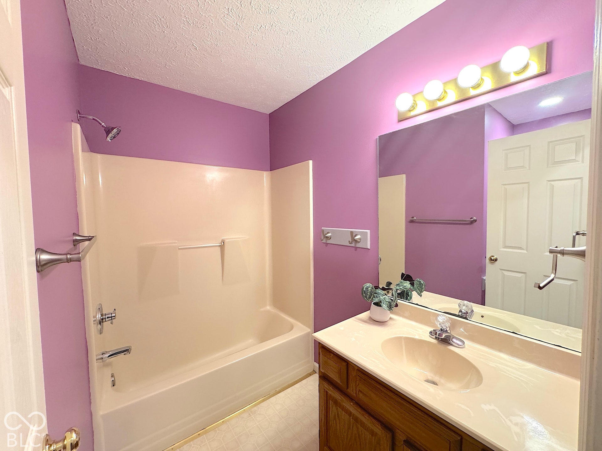 Built-in bathtub with integrated shower, single vanity with integrated sink, wood-finish cabinetry, and wall-mounted mirror