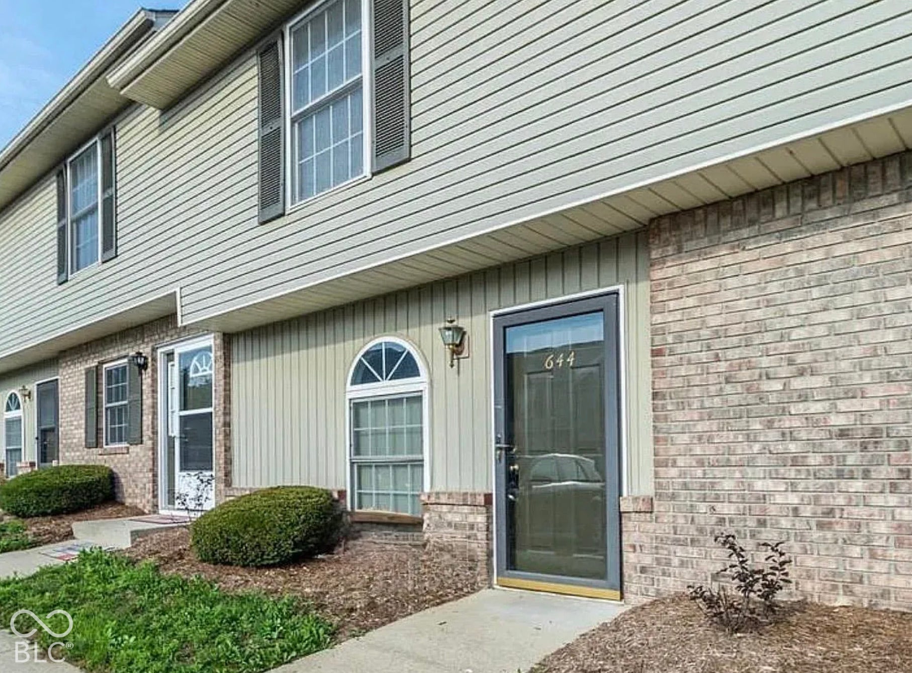 Brick and siding exterior with dark shutters, arched window, and concrete walkway