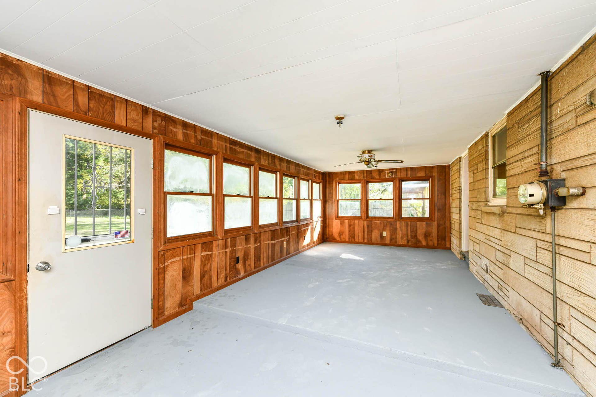 6401 Orinoco Avenue, Indianapolis, IN 46227 Enclosed porch featuring wood paneling, multiple windows, a ceiling fan, and concrete flooring