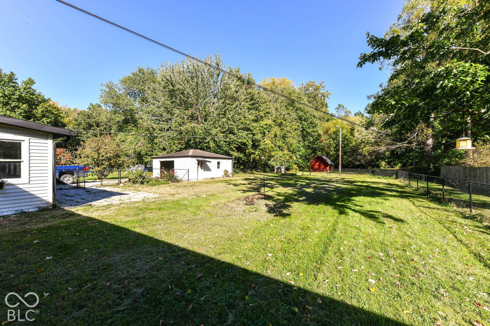 6401 Orinoco Avenue, Indianapolis, IN 46227 Expansive grassy yard with mature trees, featuring a detached white outbuilding, a red shed, and a chain-link fence