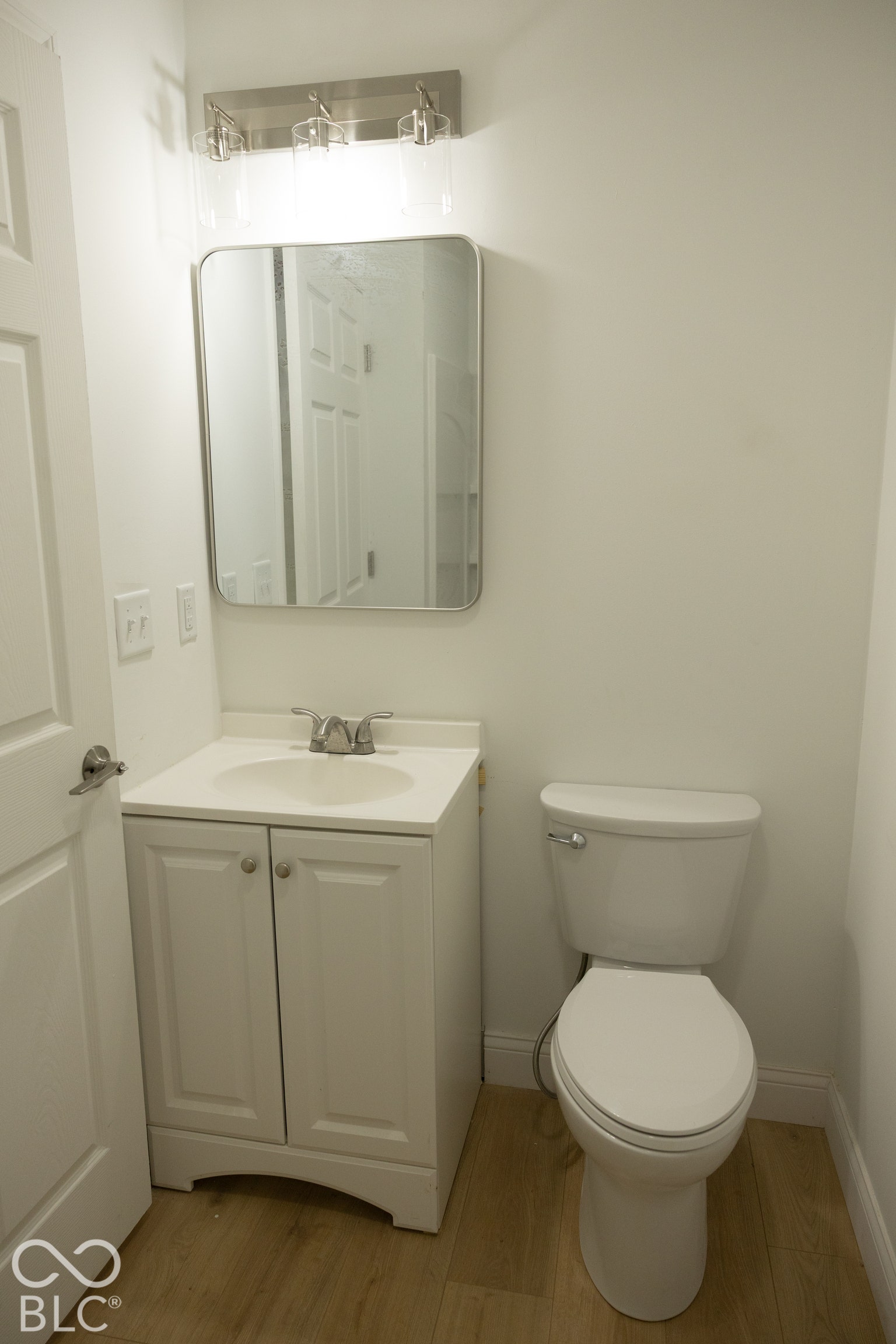 White vanity with integrated sink, chrome faucet, and wood-finish flooring