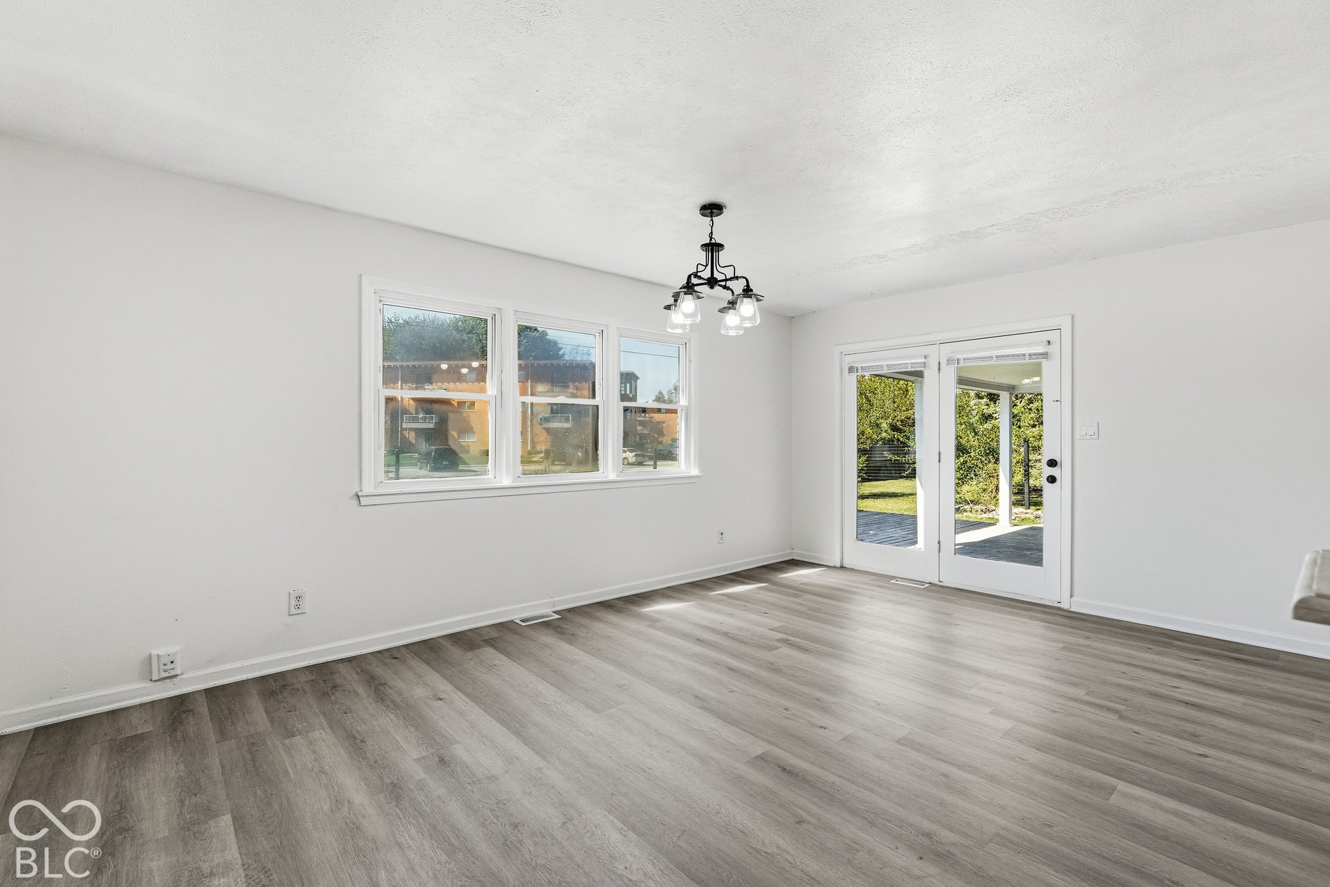 Wood-finish flooring, white walls, multiple windows, double glass doors, and a chandelier with frosted glass shades