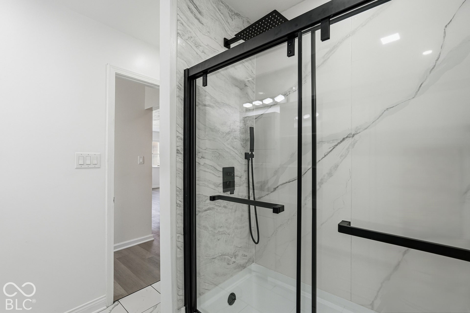 Frameless glass shower enclosure with matte black hardware, integrated rainfall showerhead, and white marble-look wall tile
