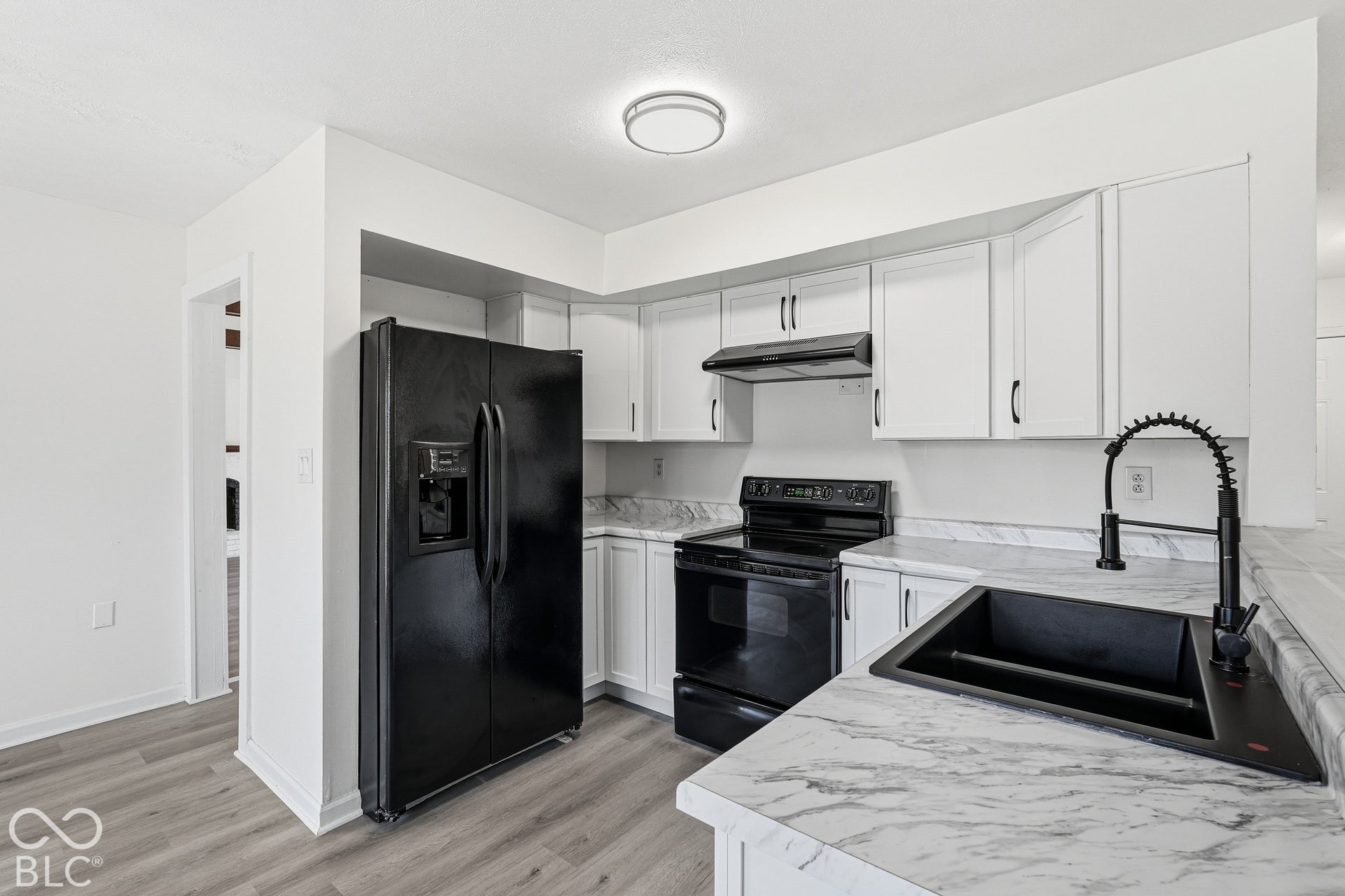 Kitchen featuring light cabinetry, dark appliances, wood-finish flooring, and a stone-finish countertop with an integrated sink
