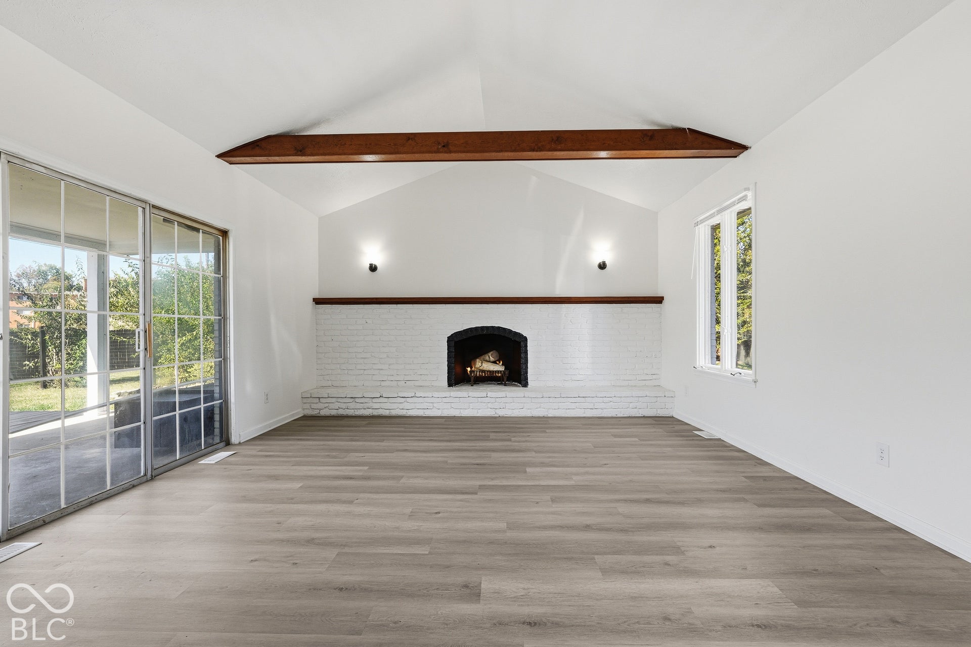 Vaulted ceilings with exposed wood beams, wood-finish flooring, white brick fireplace with mantel, and large sliding glass doors