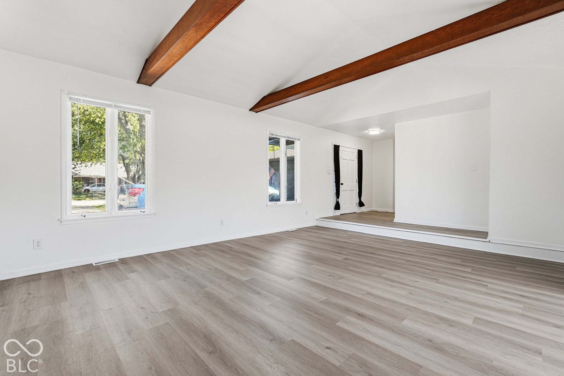 Vaulted ceiling with exposed wood beams, light wood-finish flooring, and white painted walls