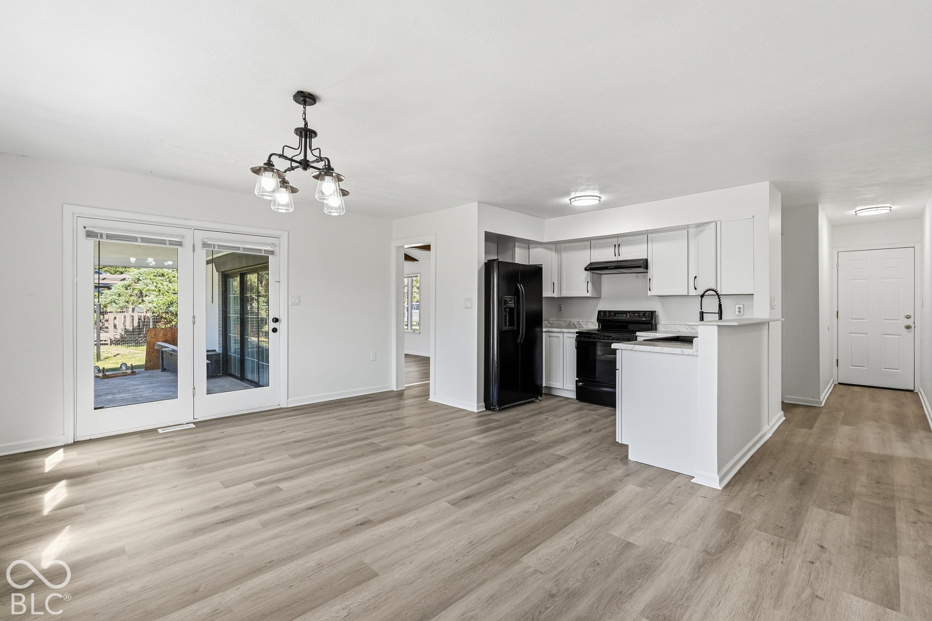 Open-concept living space featuring wood-finish flooring, a contemporary chandelier, and white French doors