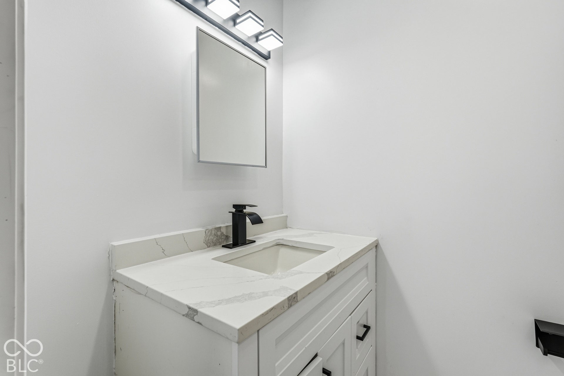 Modern bathroom vanity featuring a white finish with ample storage, light marble-finish countertop, rectangular undermount sink, and matte black faucet
