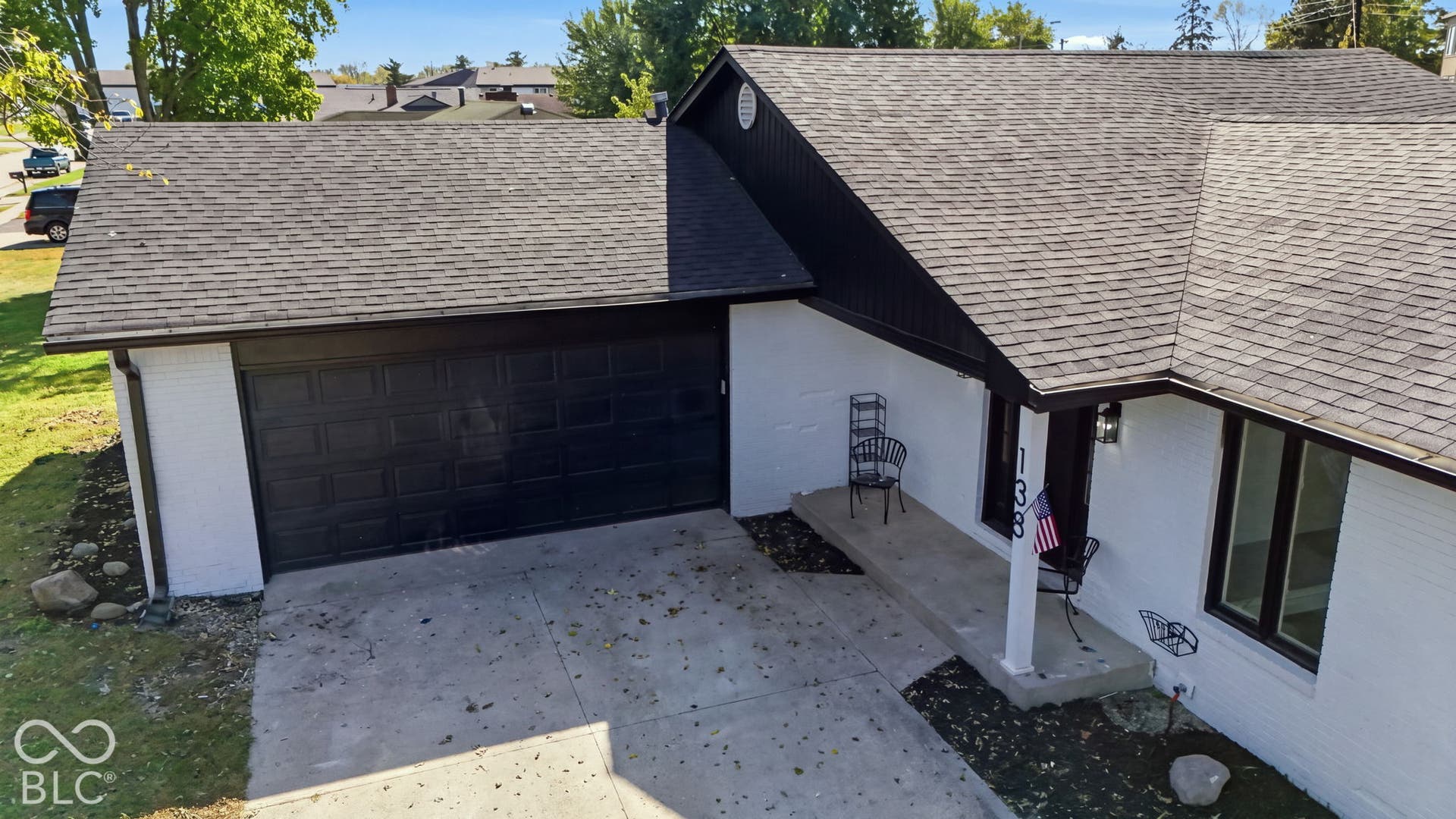 White brick exterior with dark trim accents, asphalt shingle roofing, attached two-car garage, and a concrete driveway