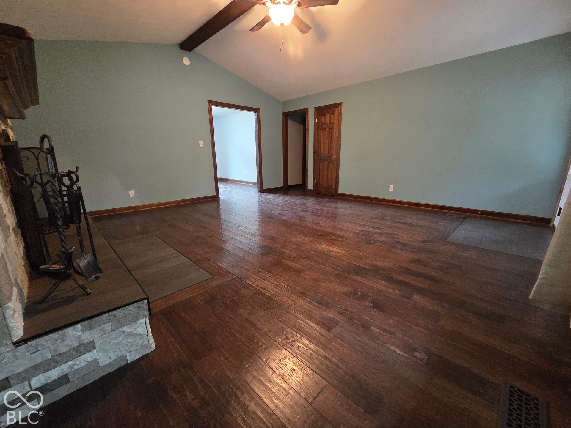 6614 Weil Drive, Brownsburg, IN 46112 Cathedral ceiling with exposed wood beam, hardwood-finish flooring, stone-clad fireplace with hearth, and a ceiling fan.