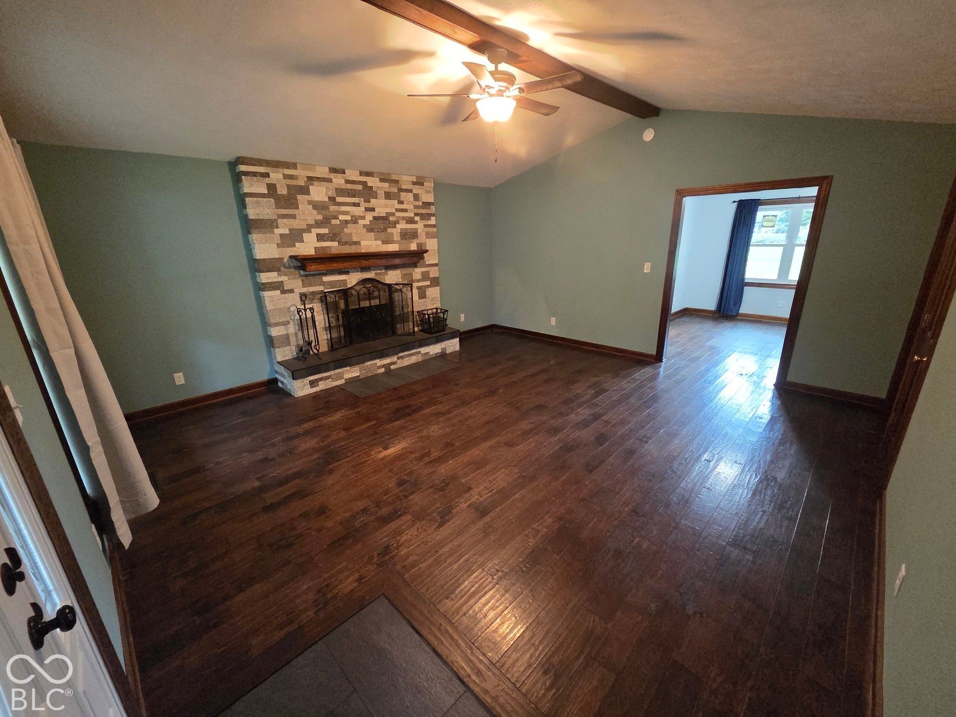 6614 Weil Drive, Brownsburg, IN 46112 Large great room with cathedral ceiling, exposed wood beam, hardwood-finish flooring, stone-clad fireplace with hearth, and ceiling fan.