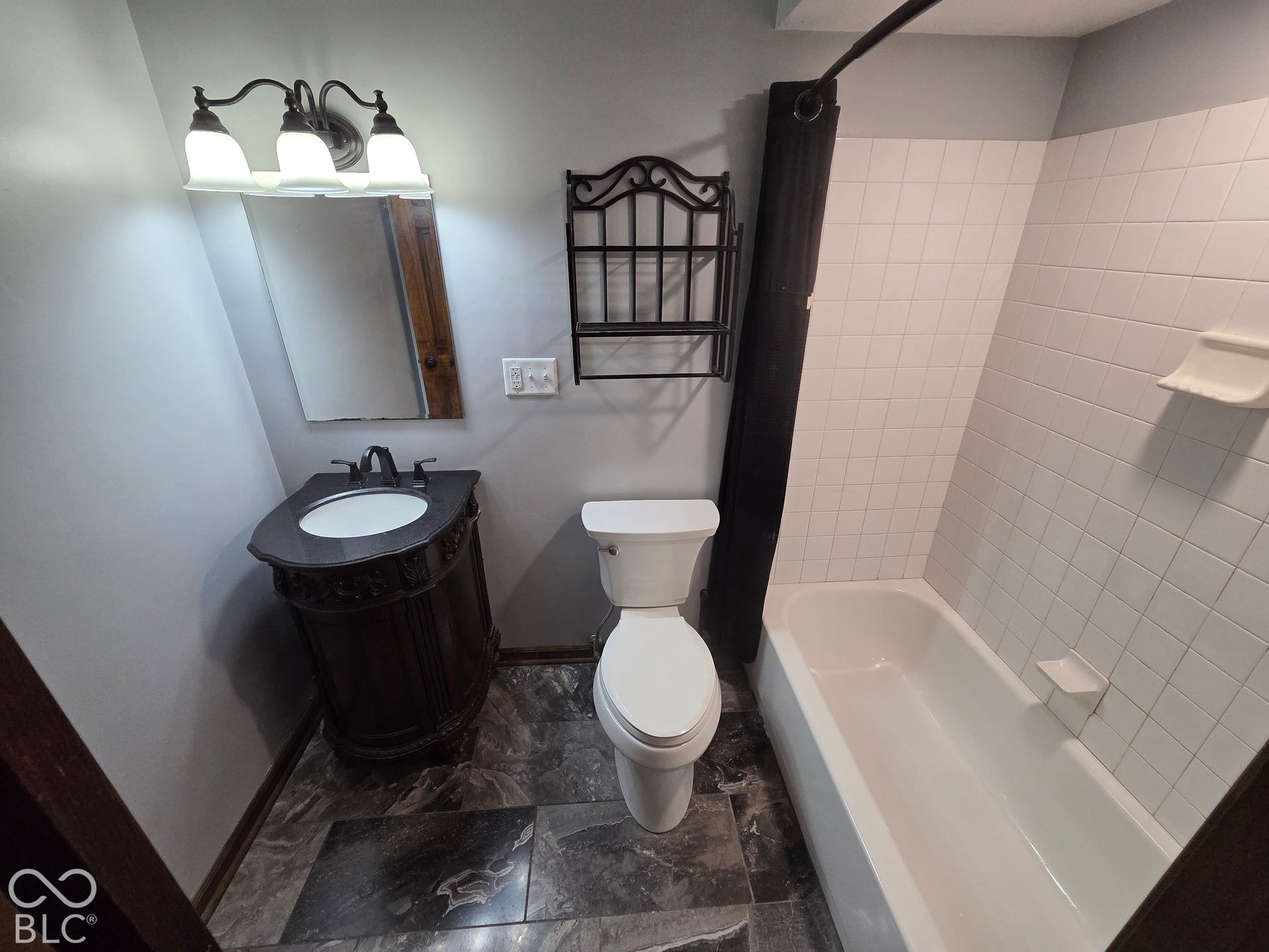 6614 Weil Drive, Brownsburg, IN 46112 Bathroom featuring a vanity with an integrated sink, a three-light fixture, white tiled shower surround, and dark patterned flooring