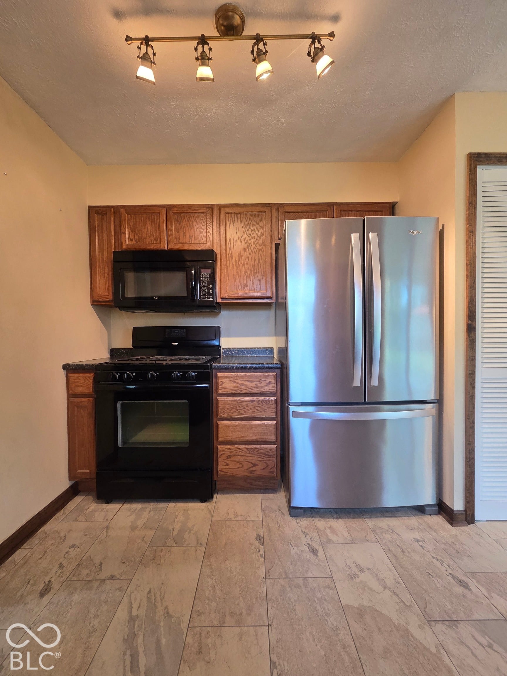 6614 Weil Drive, Brownsburg, IN 46112 Stainless steel refrigerator, black range, black microwave, wood cabinetry, and track lighting