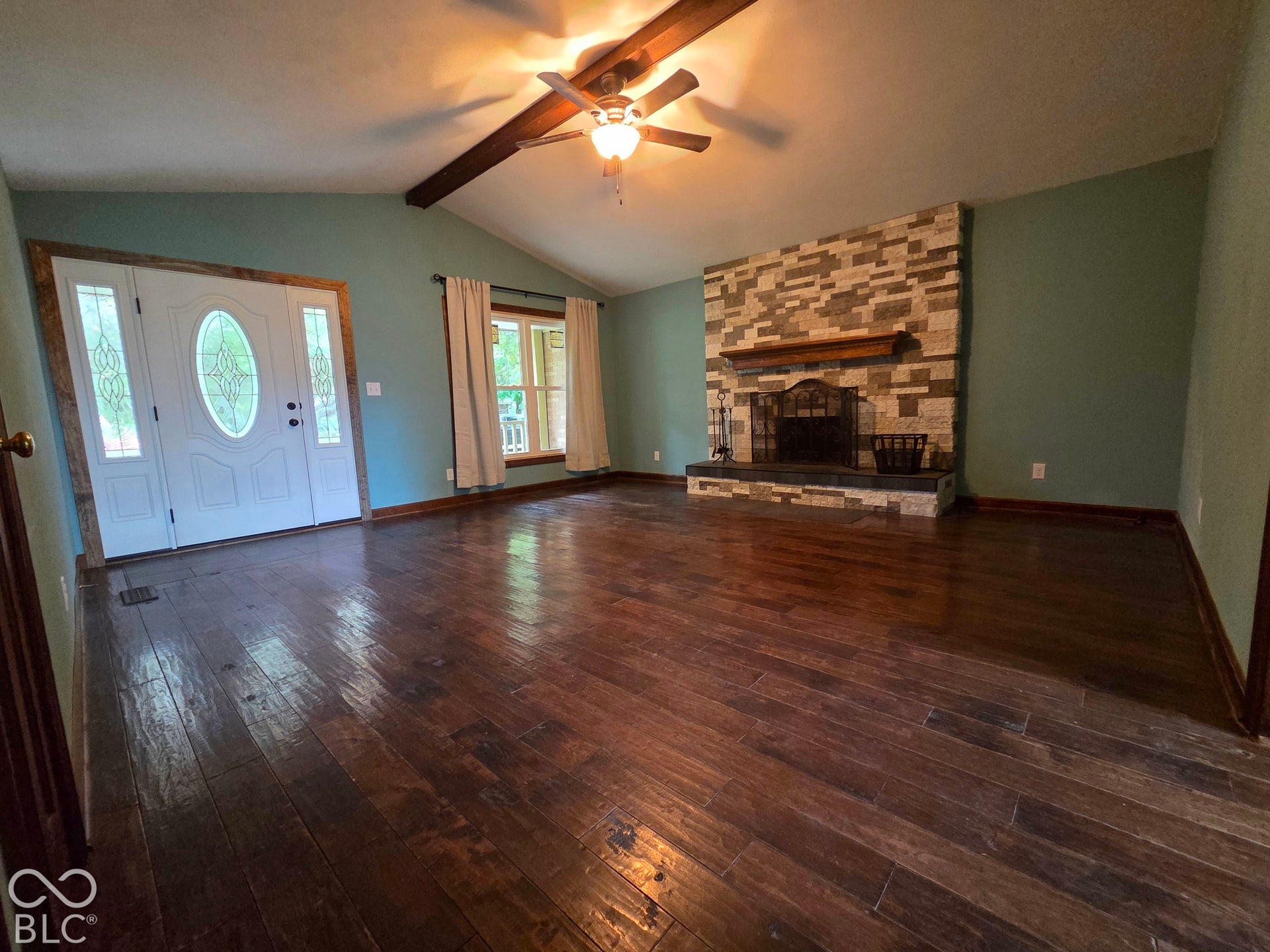 6614 Weil Drive, Brownsburg, IN 46112 Spacious living area featuring wood-finish flooring, a stone-clad fireplace, cathedral ceiling with exposed beam, and a ceiling fan.