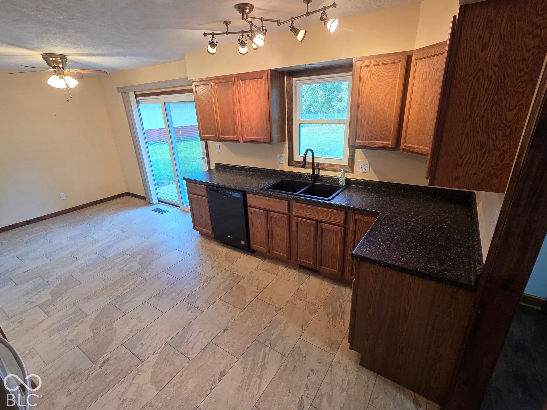 6614 Weil Drive, Brownsburg, IN 46112 Kitchen and dining area featuring wood-finish cabinetry, dark countertops, a double basin sink with a black faucet, and a sliding glass door leading to the exterior