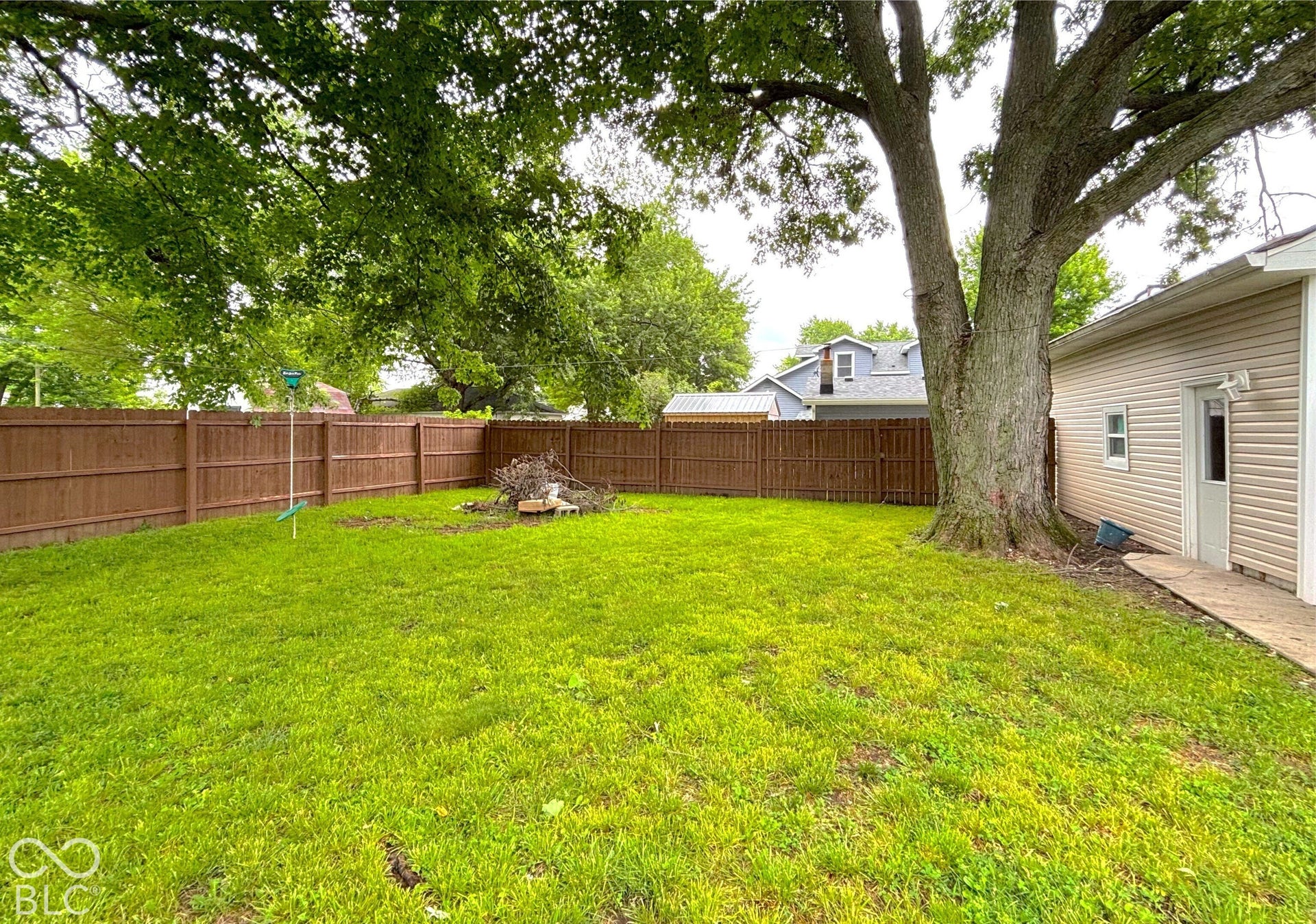 311 B Street S, Thorntown, IN 46071 Expansive grassy yard with a mature tree, wood privacy fencing, a concrete pathway, and a detached building with siding exterior