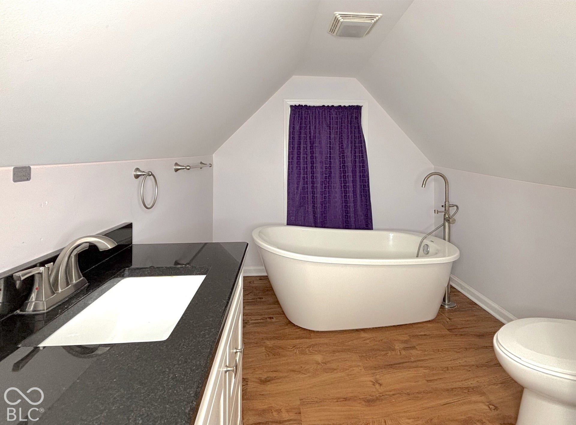 311 B Street S, Thorntown, IN 46071 Sloped ceiling bathroom featuring a standalone soaking tub with a floor-mounted faucet, a vanity with a dark countertop and undermount sink, and wood-finish flooring