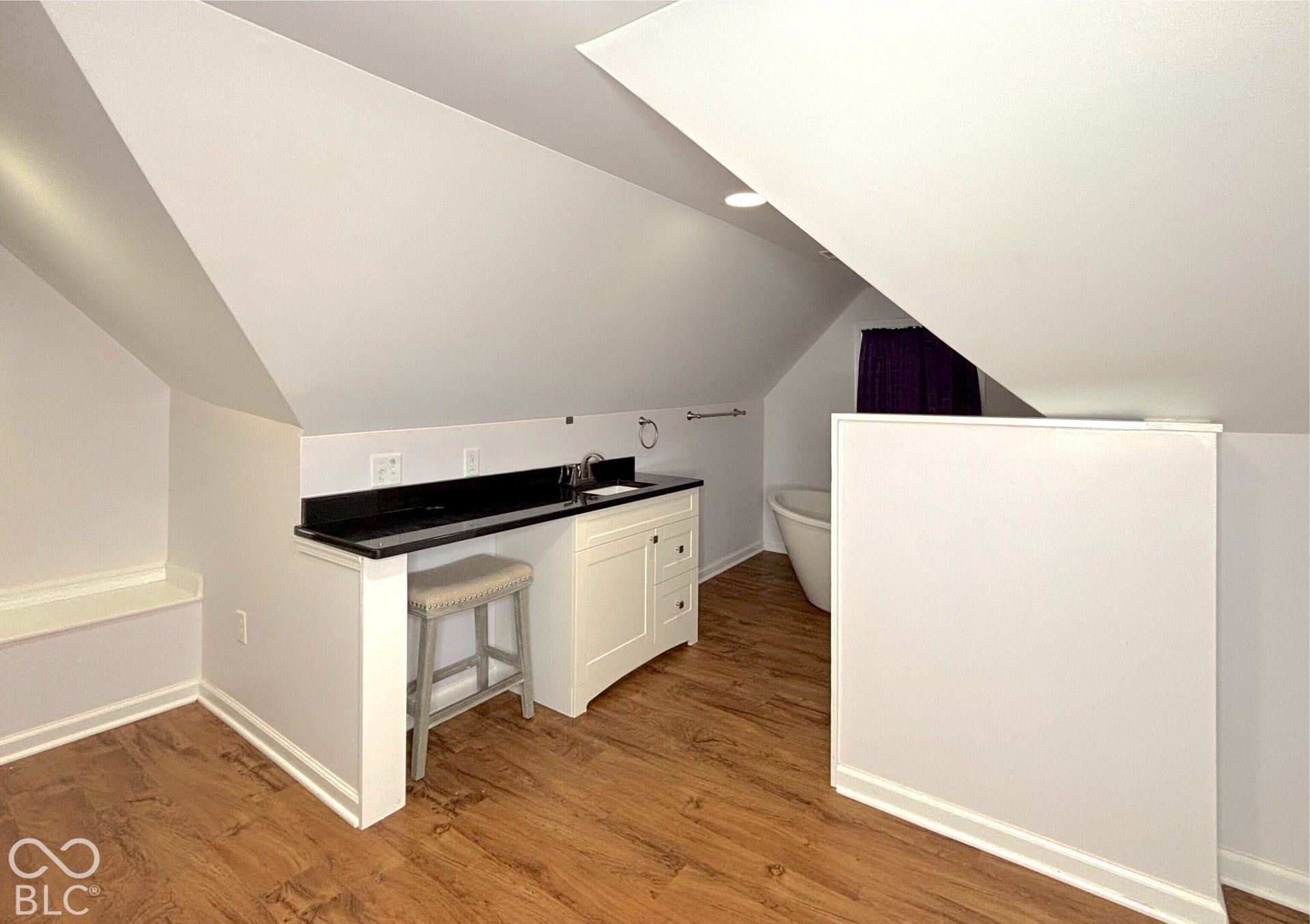 311 B Street S, Thorntown, IN 46071 Sloped ceiling bathroom featuring a standalone soaking tub with a floor-mounted faucet, a vanity with a dark countertop and undermount sink, and wood-finish flooring
