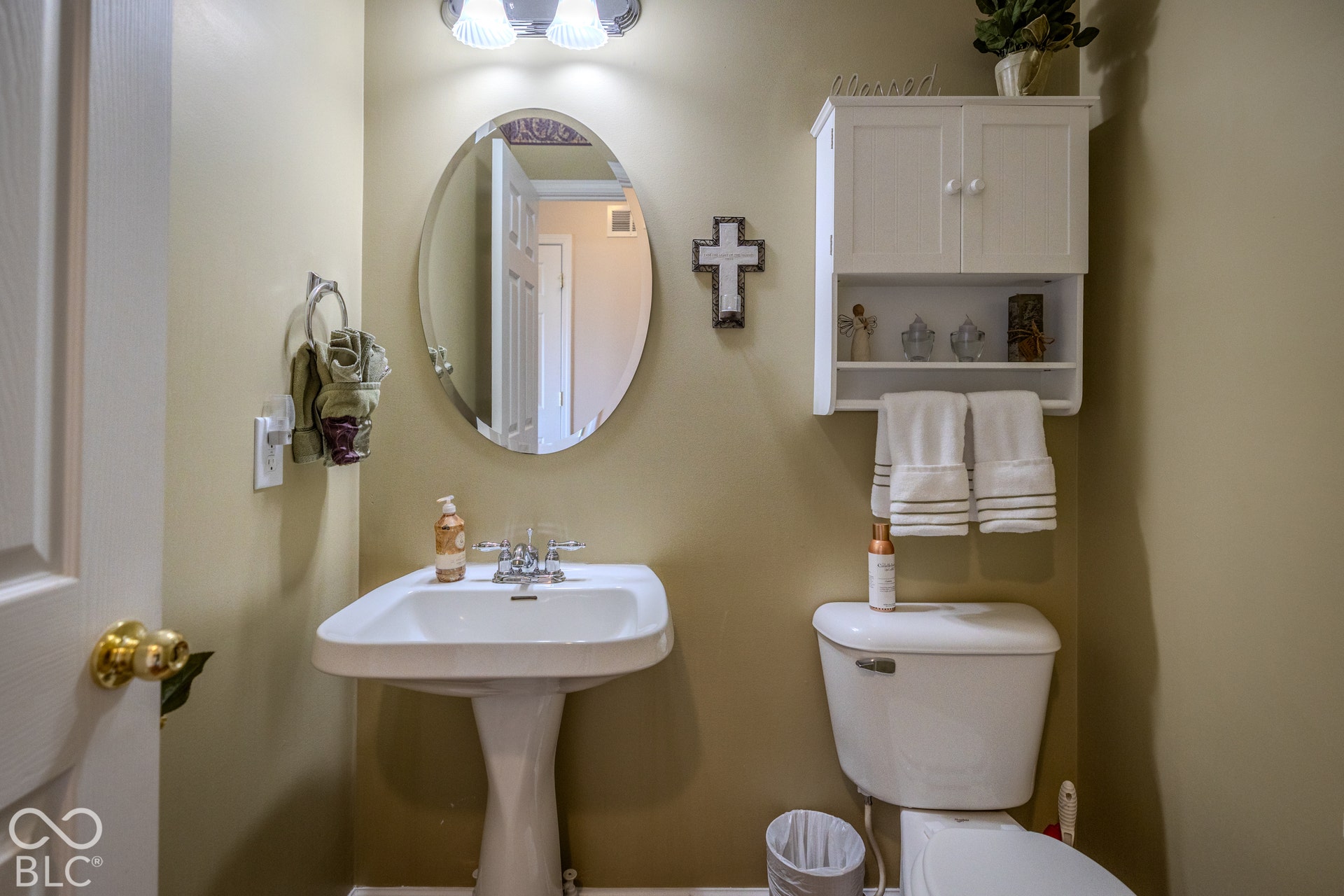 12046 Cowboys, Fishers, IN 46037 The powder room features a pedestal sink with chrome fixtures, oval wall mirror, wall-mounted vanity light, and white wall cabinet with open shelving