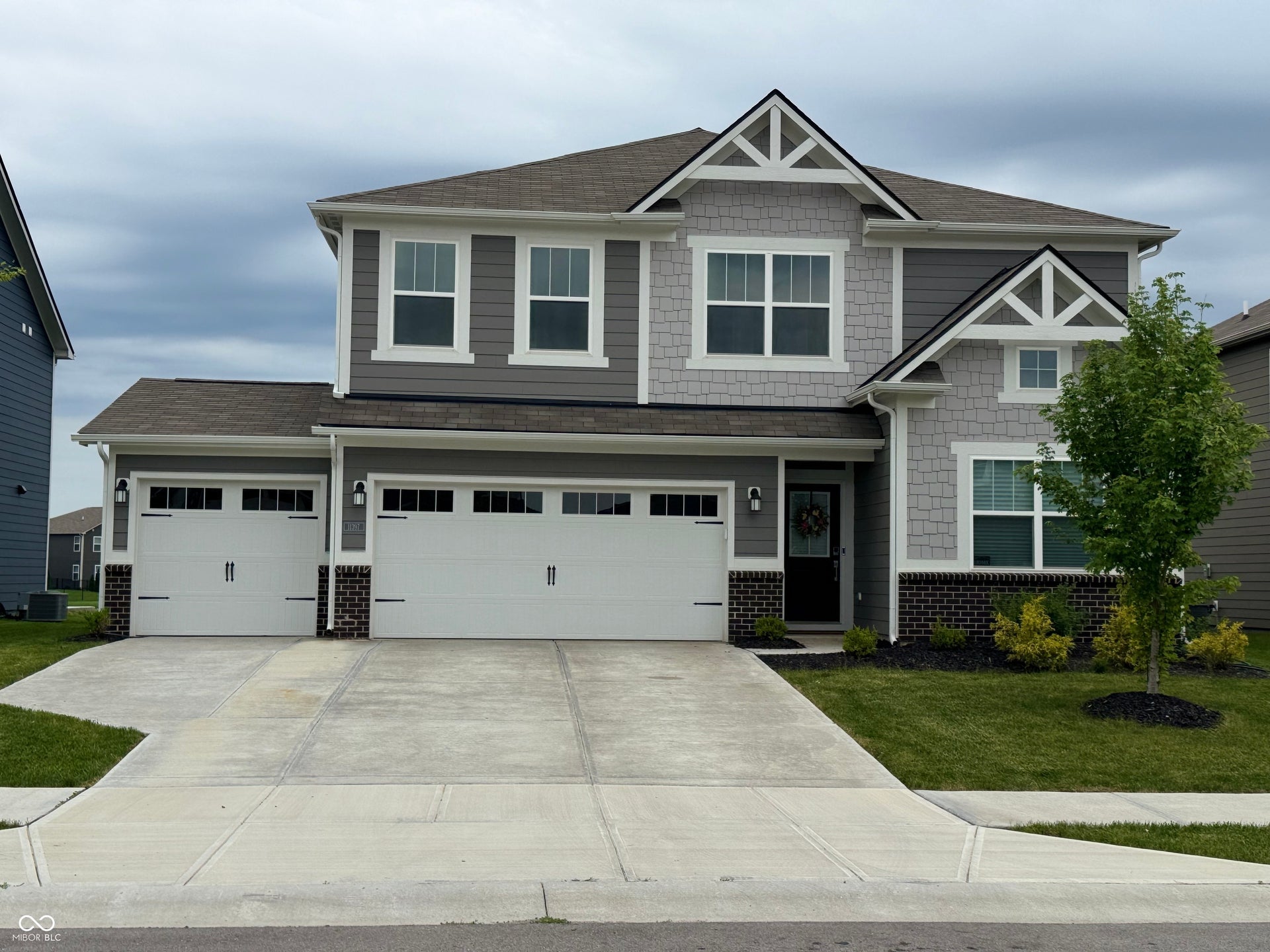 Contemporary two-story residence featuring a two-car garage with overhead lighting, a dark gray front door, and a combination of shingle siding and brick accents