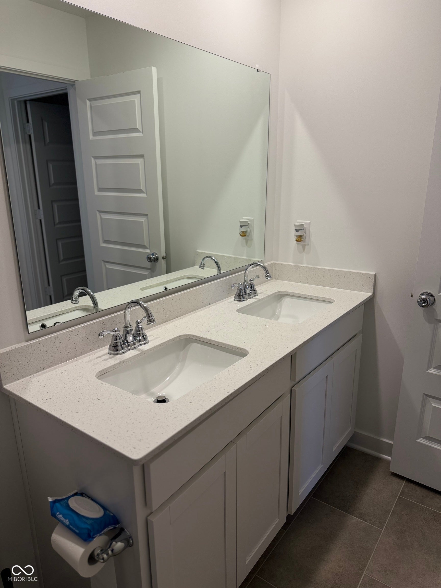 Dual vanity featuring white shaker-style cabinetry, white countertops with integrated sinks, and chrome-finish faucets