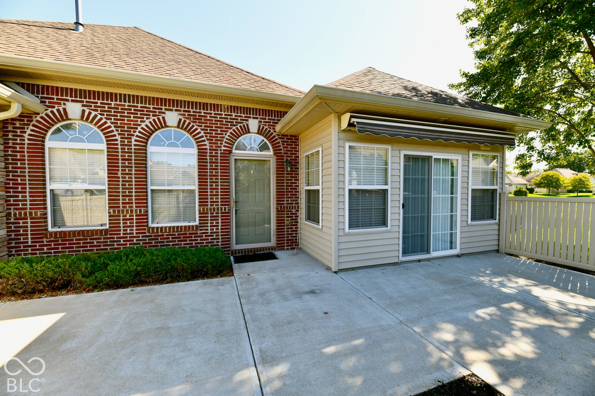6673 Avila Way, Fishers, IN 46038 Red brick exterior with arched windows, sunroom with sliding glass door, patio with concrete surface, and light-colored fencing