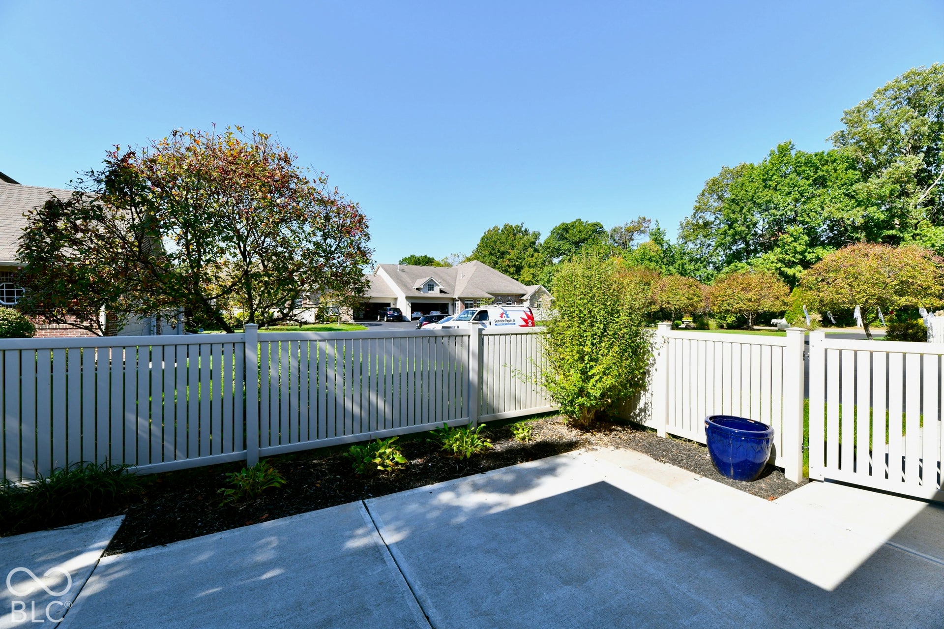 6673 Avila Way, Fishers, IN 46038 Concrete patio with a white picket fence and gate, surrounded by established landscaping and mature trees