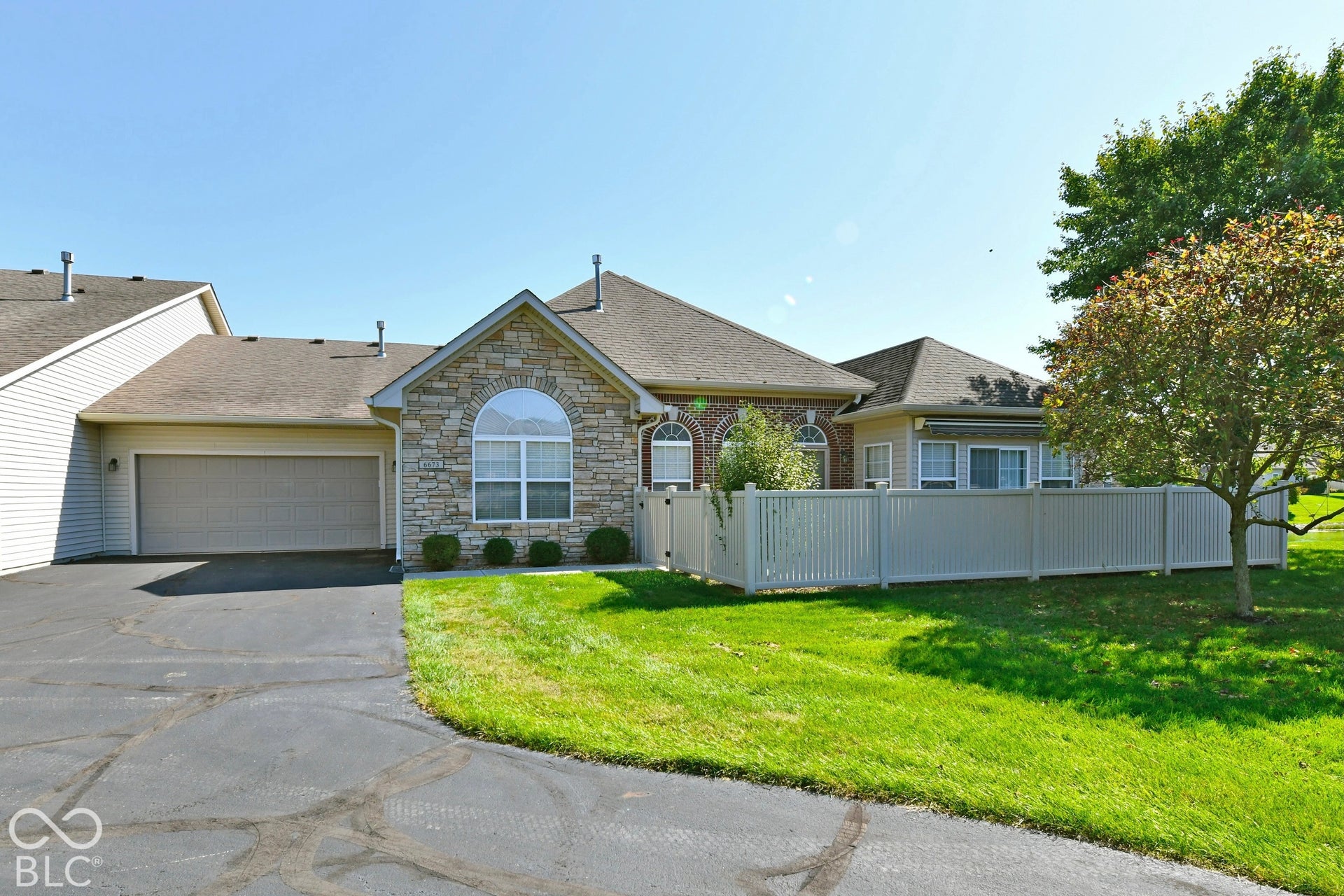 6673 Avila Way, Fishers, IN 46038 Stone and brick exterior with an arched window, attached garage, and white privacy fencing
