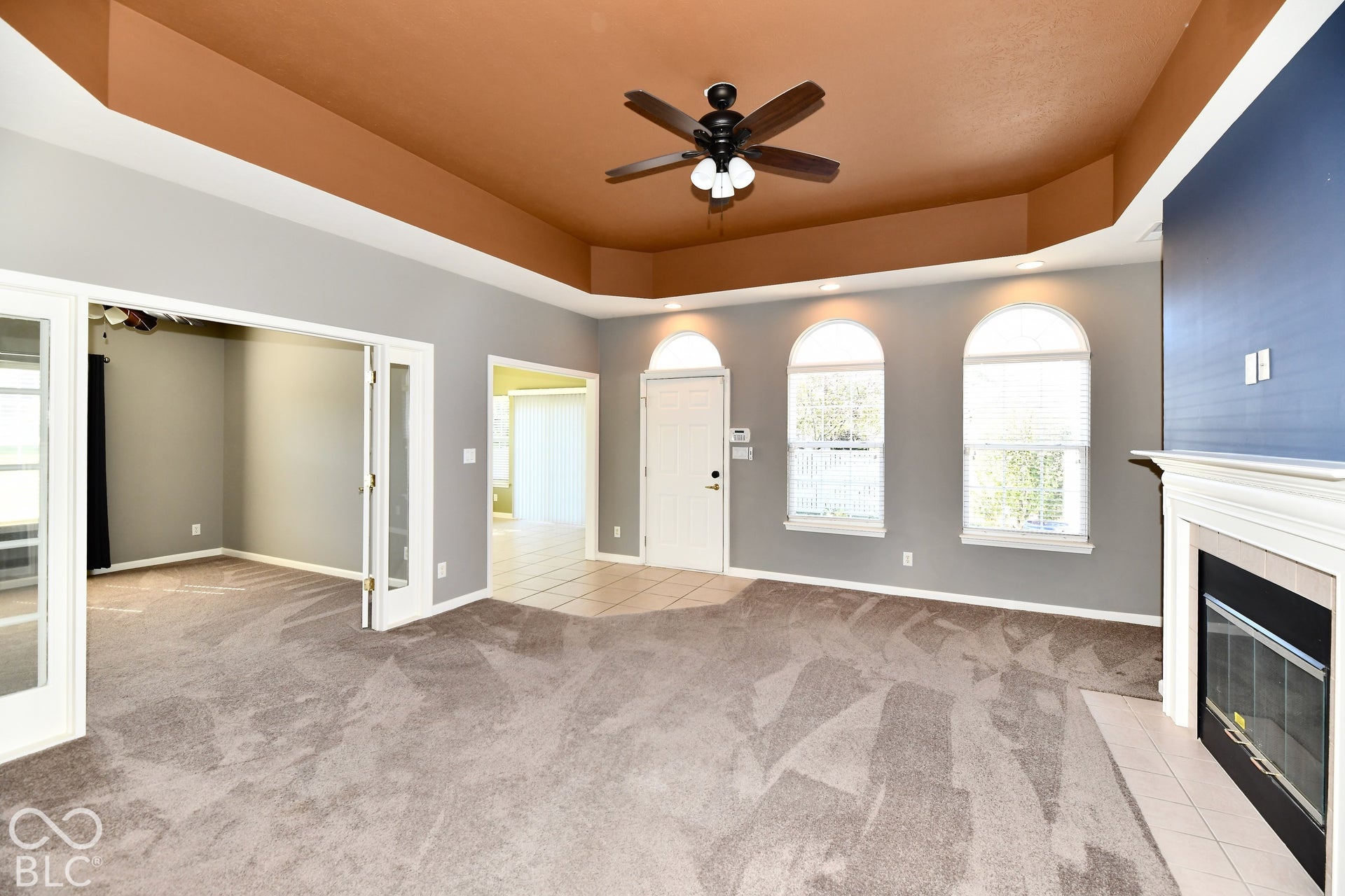 6673 Avila Way, Fishers, IN 46038 Tray ceiling with integrated lighting, a ceiling fan, three arched windows, a fireplace with a white mantel, and French doors