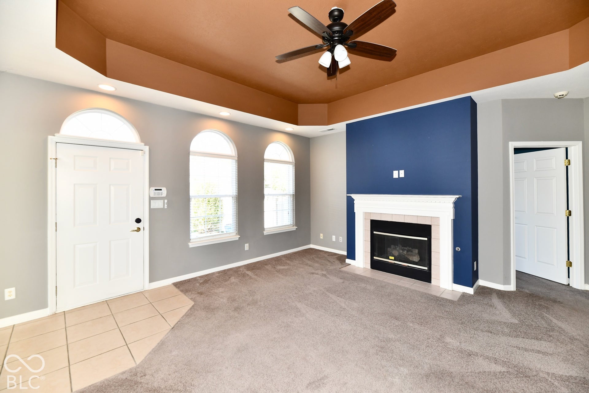 6673 Avila Way, Fishers, IN 46038 Living space featuring a white mantel fireplace, a ceiling fan, arched windows, and tiled flooring at the entry